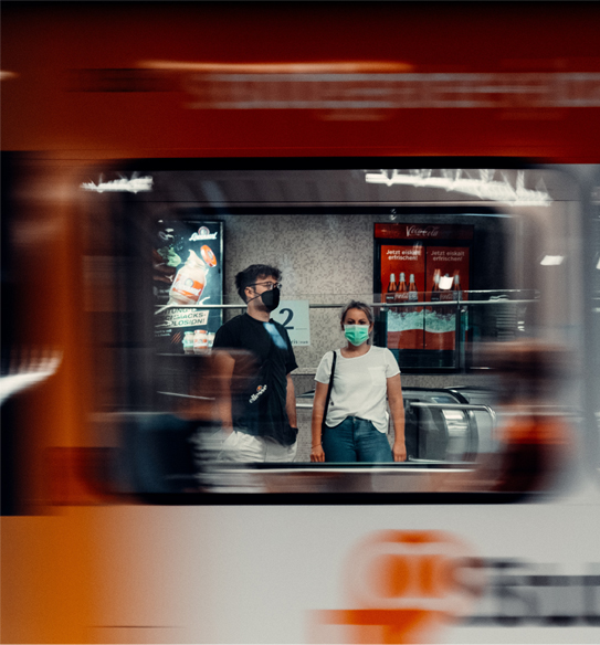 Two people wearing masks waiting for the train reflected in a mirror